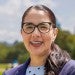 Professional headshot of Dr. Karen Lozano smiling in a navy blazer, polka dot shirt, and glasses with her hair pulled back and a sunny green park in the background.